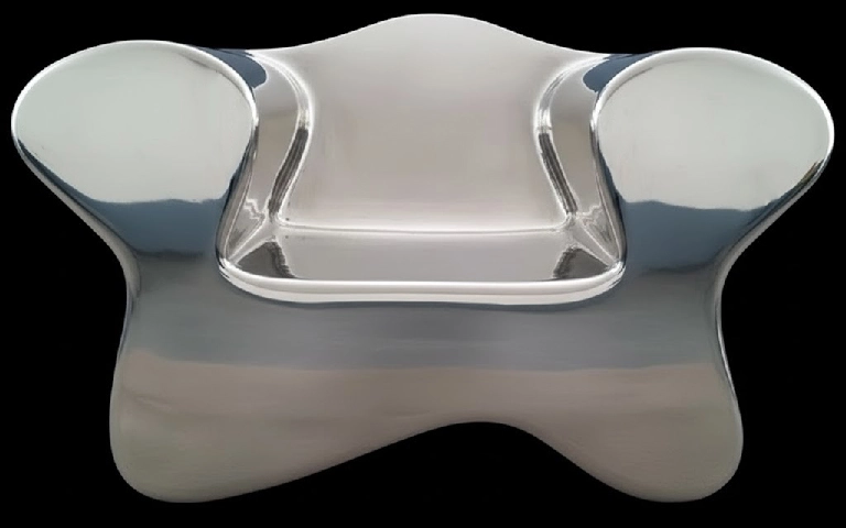 Borderlast-Ghost-inox-poli Cette image présente un fauteuil sculptural d'une originalité saisissante, réalisé en acier. La forme du fauteuil est à la fois organique et abstraite, inspiré de l'iconique fauteuil Club, plus stylisée ou une forme biomorphique. Le dossier s'élève en une courbe douce au centre, flanqué de deux accoudoirs qui s'évasent de manière asymétrique, donnant à l'ensemble une allure presque vivante. La surface de l'acier présente une patine complexe et nuancée. Des tons de gris argenté dominent, parsemés de reflets bleutés et de zones plus sombres qui créent une texture riche et profonde. Cette finition donne l'impression que le fauteuil a été façonné par les éléments, comme un objet ancien remonté des profondeurs marines. L'assise est formée par un creux subtil dans la structure, invitant à s'y installer tout en maintenant l'intégrité sculpturale de l'œuvre. Les bords du fauteuil sont délicatement arrondis, adoucissant la rigidité naturelle du métal. La lumière joue sur les courbes et les creux du fauteuil, créant un jeu d'ombres et de reflets qui accentue sa dimensionnalité et sa présence dans l'espace. Chaque angle offre une nouvelle perspective sur ses formes fluides. Ce fauteuil transcende sa fonction utilitaire pour devenir une véritable œuvre d'art. Il défie les conventions du design mobilier traditionnel, fusionnant la robustesse de l'acier avec une esthétique presque onirique. C'est une pièce qui invite autant à la contemplation qu'à l'utilisation, brouillant la frontière entre sculpture et meuble fonctionnel. This image features a strikingly original sculptural armchair crafted from steel. The chair's form is both organic and abstract, inspired by the iconic Club chair but stylized into a biomorphic shape. The backrest rises in a gentle curve at the center, flanked by two asymmetrical armrests that give the piece an almost lifelike appearance. The surface of the steel exhibits a complex and nuanced patina. Shades of silvery gray dominate, interspersed with bluish reflections and darker areas that create a rich and deep texture. This finish gives the impression that the chair has been shaped by the elements, resembling an ancient artifact unearthed from the depths of the sea. The seat is formed by a subtle hollow within the structure, inviting one to sit while maintaining the sculptural integrity of the piece. The edges of the chair are delicately rounded, softening the inherent rigidity of the metal. Light plays on the curves and hollows of the chair, creating a play of shadows and reflections that accentuate its dimensionality and presence in space. Each angle offers a new perspective on its fluid forms. This chair transcends its utilitarian function to become a true work of art. It challenges conventions of traditional furniture design, merging the robustness of steel with an almost dreamlike aesthetic. It is a piece that invites contemplation as much as use, blurring the boundaries between sculpture and functional furniture.